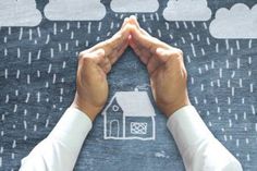 someone holding their hands up in front of a house drawn on the ground with rain coming down