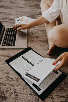 a woman is sitting on the floor with her laptop and papers in front of her