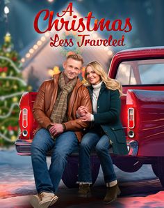 a man and woman sitting on the back of a red truck in front of a christmas tree