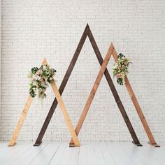 three wooden wedding archs with flowers and greenery on them in front of a white brick wall