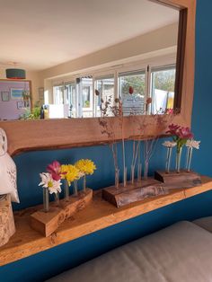 flowers are arranged in vases on a wooden shelf near a large mirror and blue wall