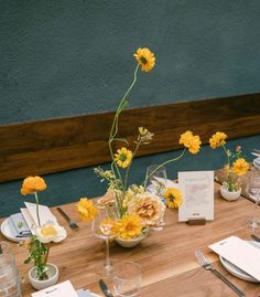 the table is set with yellow flowers and place settings