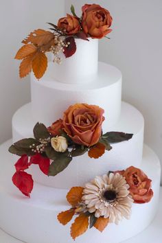 a three tiered white cake with flowers on the top and leaves on the bottom