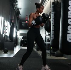 a woman wearing black boxing gloves in a gym with punching mitts on her hands