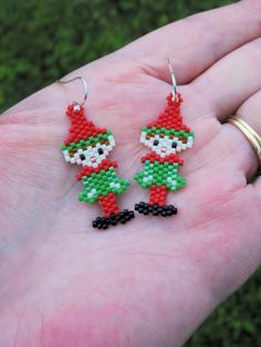 a hand holding a pair of beaded christmas elf earrings on it's palm