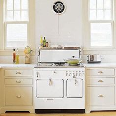 a white stove top oven sitting inside of a kitchen next to two windows and wooden floors