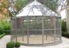 a large bird cage in the middle of a garden with trees and bushes around it