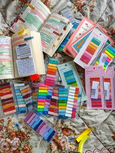 there are many different colored pencils on this bed spread with books and paper clips