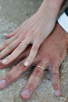 a close up of two people wearing wedding rings on their hands with sand in the background