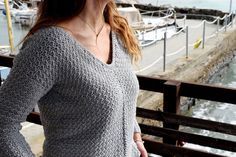 a woman standing on a pier next to the ocean with boats in the water behind her