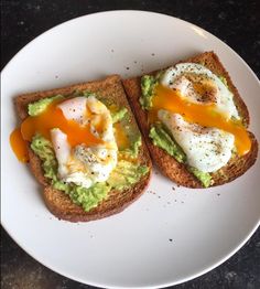 two pieces of toast with avocado and an egg on top sitting on a white plate