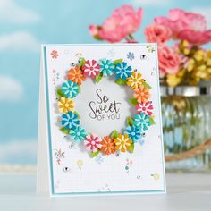 a card with flowers on it sitting next to a vase filled with pink and yellow flowers