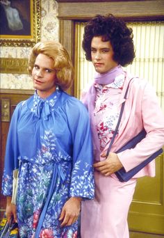 two people standing next to each other in front of a door wearing blue and pink outfits