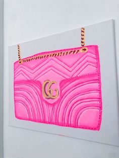 a pink handbag hanging on the side of a white wall with gold lettering and a g logo