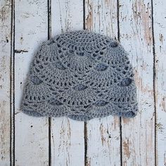 a gray crocheted hat sitting on top of a wooden floor next to a white wall