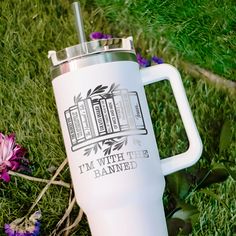 a white coffee mug sitting on top of green grass next to purple and pink flowers