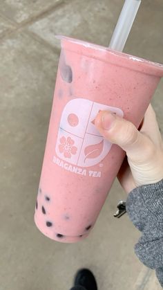 a person holding up a pink drink with black dots on the side and a straw in it