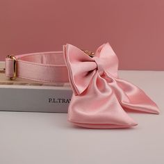 a pink dog collar with a large bow on it's side, sitting next to a book