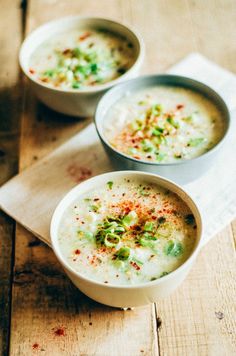 two white bowls filled with soup on top of a wooden table next to a napkin