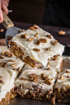 someone is cutting into a carrot cake with white frosting and pecans on top