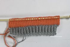 an orange and gray crocheted object with a wooden knitting needle on the end