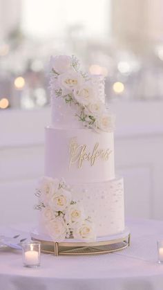 a wedding cake with white flowers and gold lettering on it is sitting on a table