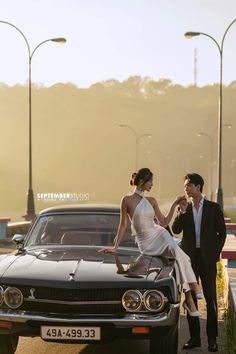 a man standing next to a woman in front of a black car on the road