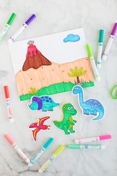 some crayons and markers are laying on a table with an image of dinosaurs