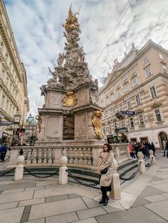 a woman sitting on a bench in front of a fountain with gold statues and people walking around