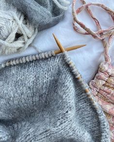 two knitting needles are next to a gray knitted blanket and some other items on a white sheet