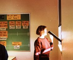 a woman standing in front of a blackboard with writing on it and another person looking up at her