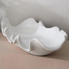 a large white bowl sitting on top of a wooden table next to a wall with a plant in it