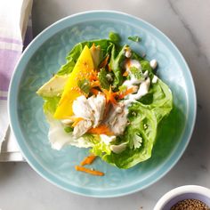 a blue plate topped with lettuce next to a white bowl filled with food