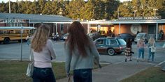 several people are walking towards a school with cars parked in the parking lot behind them