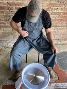 a man in overalls sitting on a chair next to a bucket with a ventilator