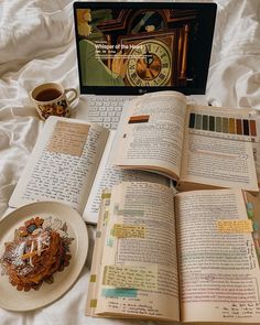 an open book sitting on top of a bed next to a plate of food and a laptop