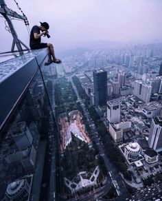 a man sitting on top of a tall building looking down at the city from above