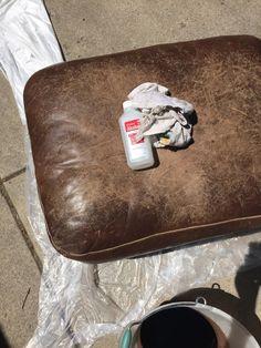 a brown leather chair sitting on top of a sidewalk next to a trash can and bucket