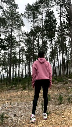 a person in a pink hoodie standing on a dirt road next to some trees