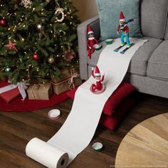 a living room with a christmas tree and elf decorations on the floor next to a roll of toilet paper