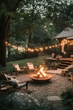 Cozy outdoor fire pit area with string lights, surrounded by wooden chairs and lush greenery. Fire Pit With Rocks Natural Stones, Fire Outside Ideas, Modern Backyard Fire Pit Ideas, Patio Area With Fire Pit, Outdoor Fire Pit Lights, Outdoor Living Lighting Ideas, Home With Backyard, Rustic Modern Backyard, Garden Design With Fire Pit