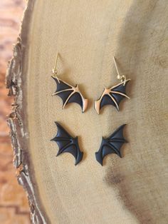 two black bat shaped earrings sitting on top of a piece of wood next to each other