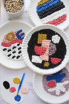 four paper plates with beaded designs on them next to paintbrushes and paints