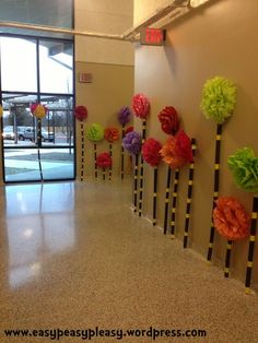 colorful paper flowers are arranged on the wall in front of an open lobby door with glass doors