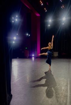 a woman is dancing in the middle of an empty room with bright lights on it