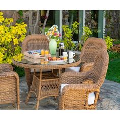 an outdoor dining set with wicker chairs and a glass top table in front of yellow flowers