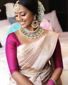 a woman in a pink and gold sari with jewelry on her neck, smiling at the camera