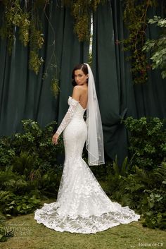 a woman wearing a wedding dress and veil standing in front of green curtained background