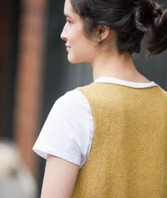 a woman wearing a yellow sweater and white shirt is looking away from the camera with her hair in a pony tail