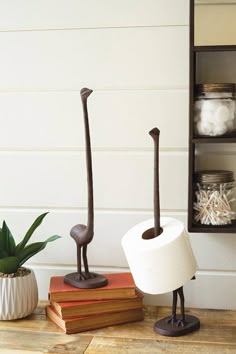 two toilet paper holders sitting on top of books next to a plant and some jars